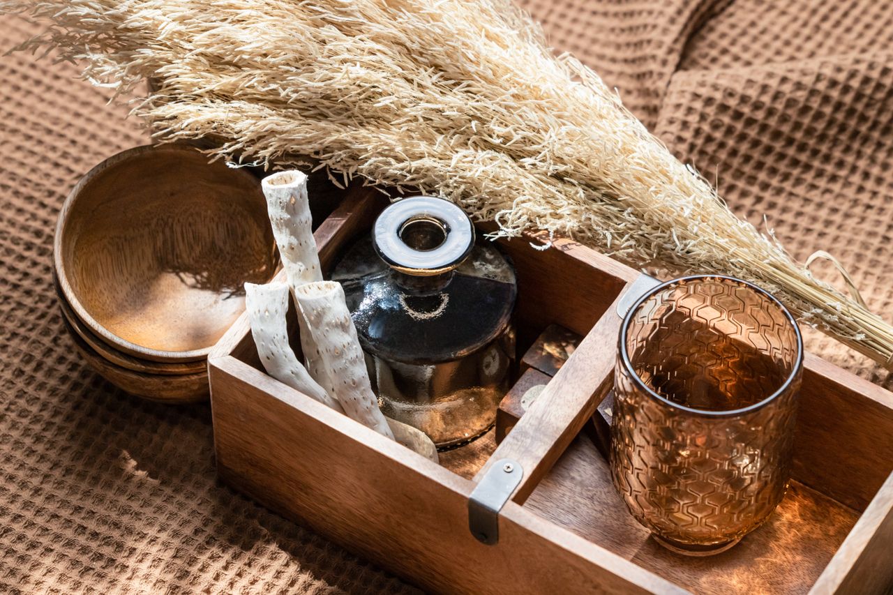 A warm arrangement featuring pampas grass, a wooden box, and glassware highlighted by soft light.