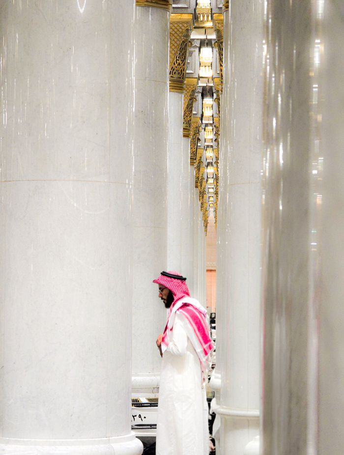 A man in traditional attire reflects quietly among the marble columns of Madinah's mosque.